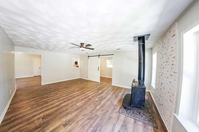 3815 Jefferson Rd, Paris, TX 75462 - unfurnished living room with a barn door, wood finished floors, a wood stove, a ceiling fan, and baseboards