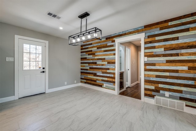 unfurnished dining area featuring baseboards, visible vents, wooden walls, and an accent wall