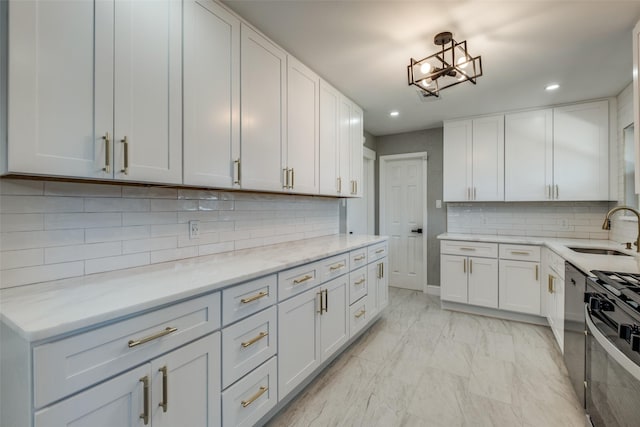 kitchen with light stone counters, a sink, gas range oven, marble finish floor, and white cabinets