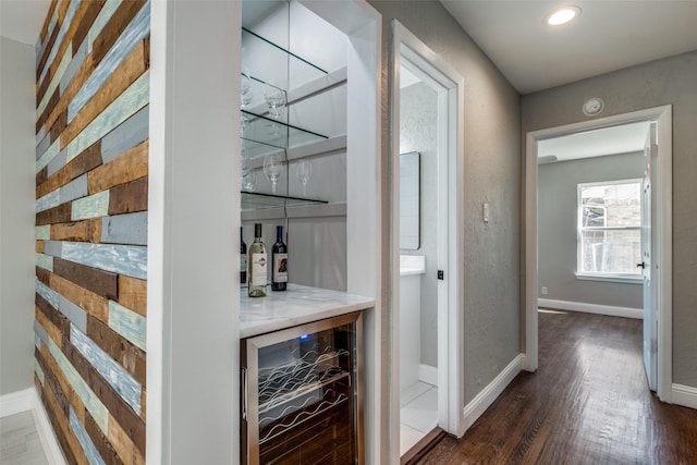 bar with a bar, baseboards, wine cooler, and dark wood finished floors