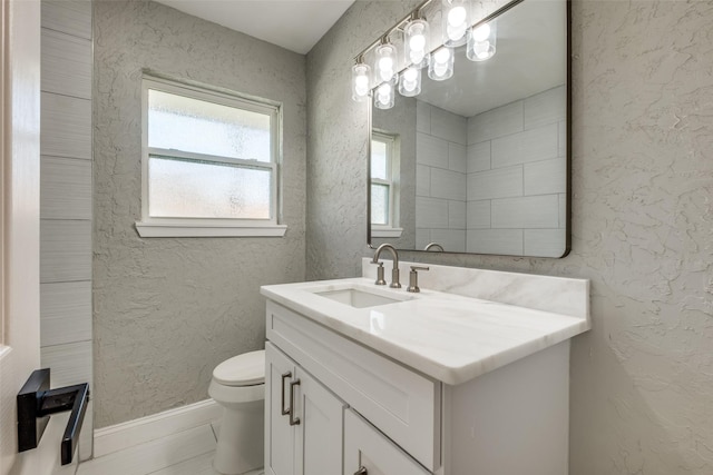 bathroom with baseboards, a textured wall, toilet, and vanity