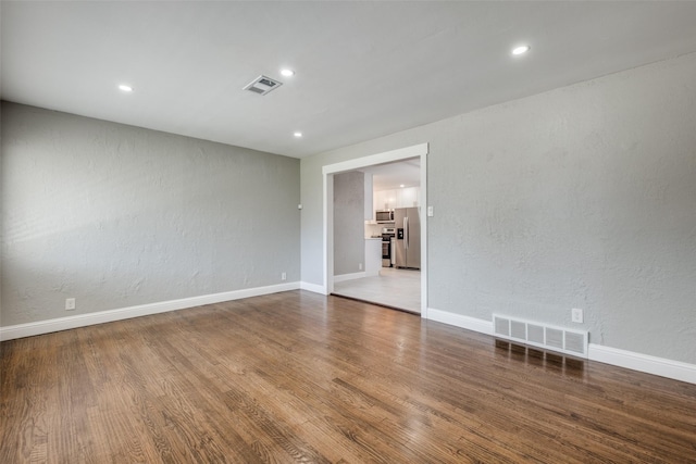 empty room with baseboards, a textured wall, visible vents, and wood finished floors