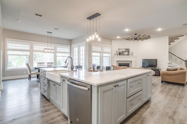 kitchen with stainless steel dishwasher, a sink, light wood-style flooring, a fireplace, and visible vents