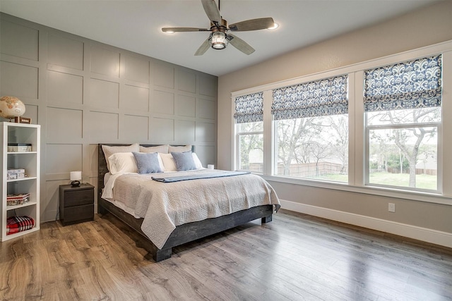 bedroom with baseboards, a ceiling fan, wood finished floors, and a decorative wall