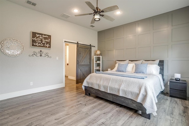 bedroom with a barn door, baseboards, visible vents, and light wood-type flooring