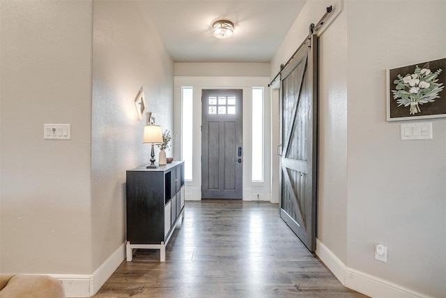 foyer entrance with a barn door, baseboards, and wood finished floors