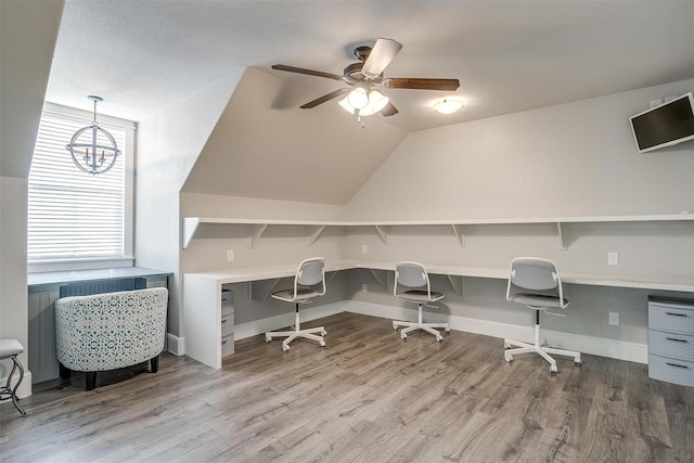 home office featuring ceiling fan with notable chandelier, baseboards, vaulted ceiling, and wood finished floors