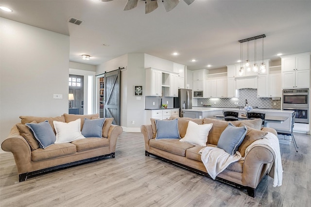 living area with a barn door, recessed lighting, visible vents, light wood-type flooring, and ceiling fan