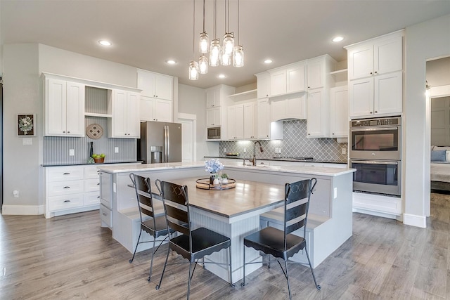 kitchen with open shelves, decorative backsplash, appliances with stainless steel finishes, and a large island with sink