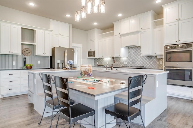 kitchen featuring tasteful backsplash, a spacious island, white cabinetry, light wood-style floors, and appliances with stainless steel finishes