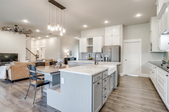 kitchen featuring a sink, open floor plan, open shelves, an island with sink, and appliances with stainless steel finishes