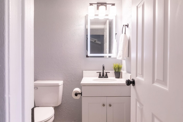 bathroom with toilet, vanity, and a textured wall
