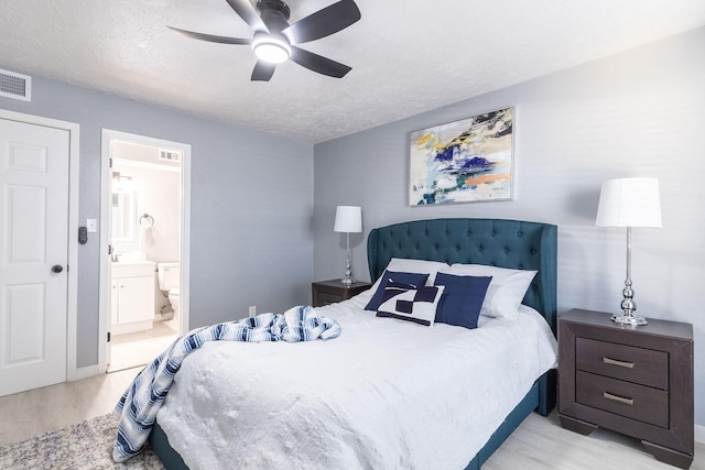 bedroom featuring light wood finished floors, ensuite bath, a textured ceiling, and ceiling fan