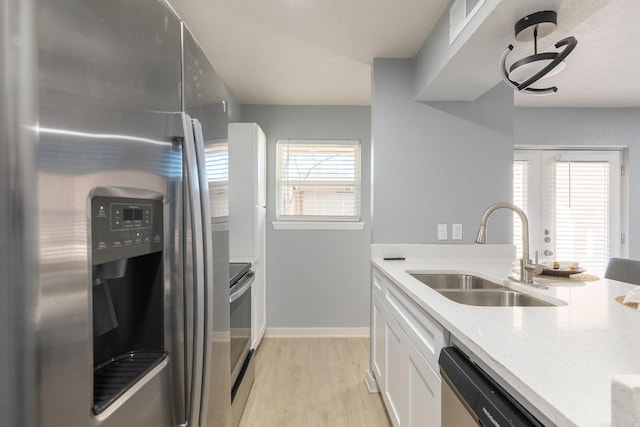 kitchen featuring stainless steel appliances, a sink, white cabinets, light wood-type flooring, and light stone counters