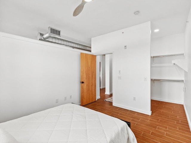 bedroom with wood finished floors, a walk in closet, baseboards, visible vents, and ceiling fan