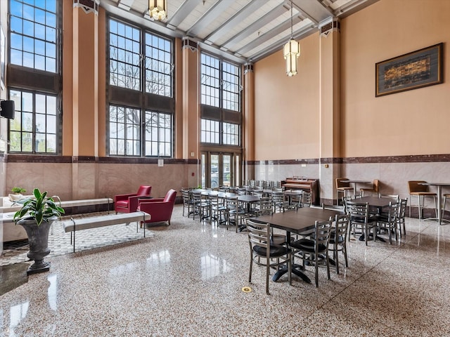 dining room featuring a towering ceiling, plenty of natural light, and wainscoting