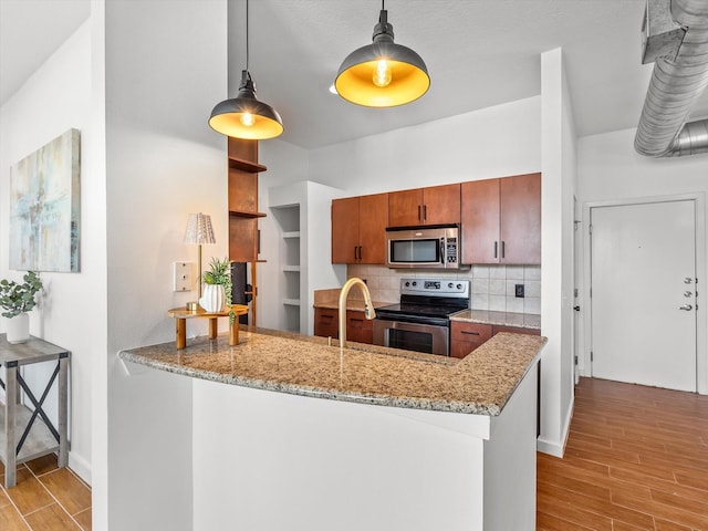 kitchen with decorative backsplash, a peninsula, stainless steel appliances, wood finish floors, and pendant lighting
