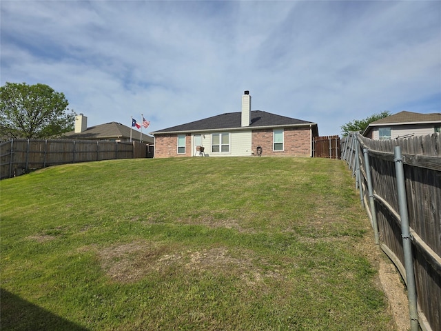 rear view of property with a chimney, a yard, a fenced backyard, and brick siding