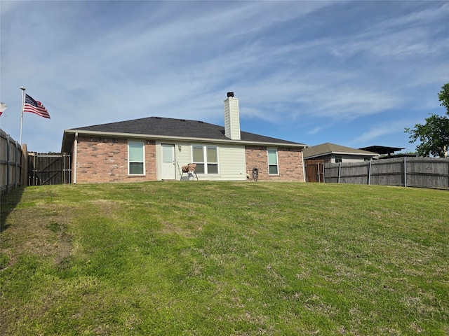 rear view of house with a chimney, a yard, a fenced backyard, and brick siding