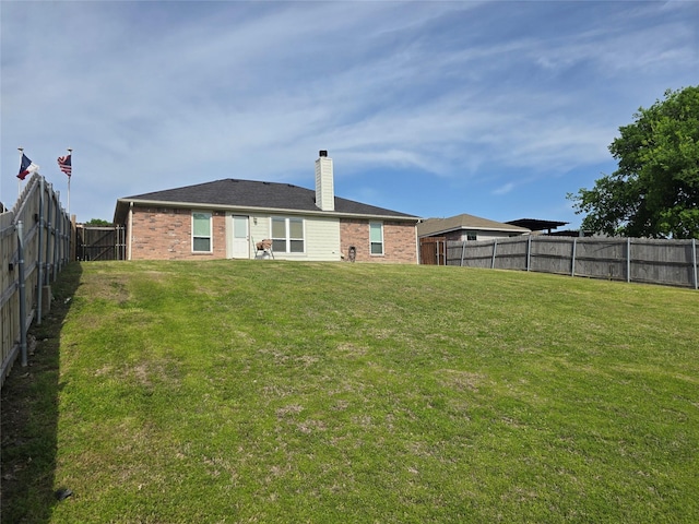 rear view of property with a yard, brick siding, a fenced backyard, and a chimney
