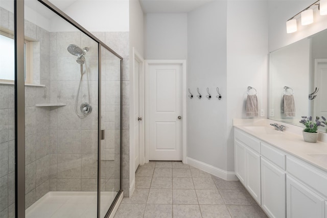 bathroom featuring baseboards, tile patterned floors, a sink, a stall shower, and double vanity