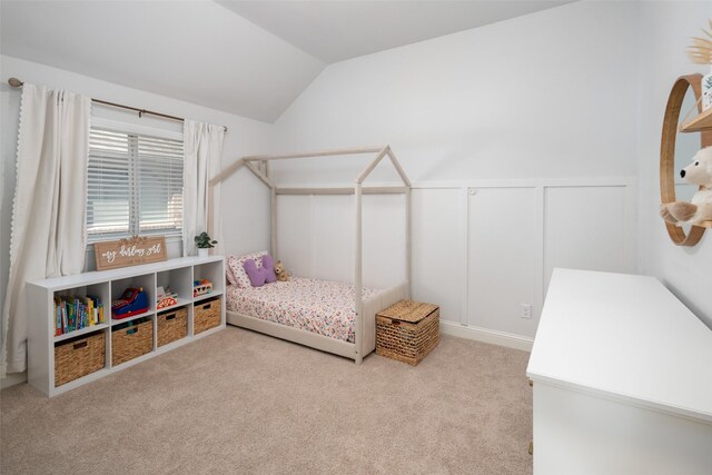 carpeted bedroom featuring a decorative wall, vaulted ceiling, and wainscoting