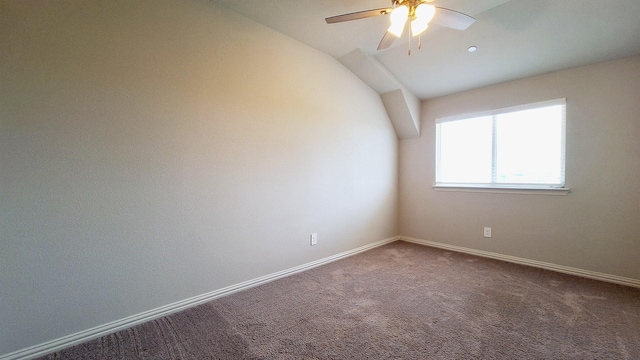 carpeted spare room with a ceiling fan, baseboards, and vaulted ceiling