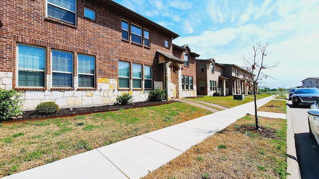 view of front of property featuring a front lawn, a residential view, stone siding, and brick siding
