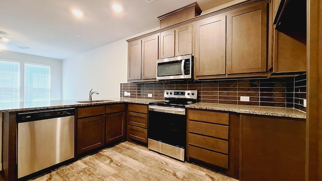 kitchen with a sink, backsplash, light stone countertops, appliances with stainless steel finishes, and a peninsula