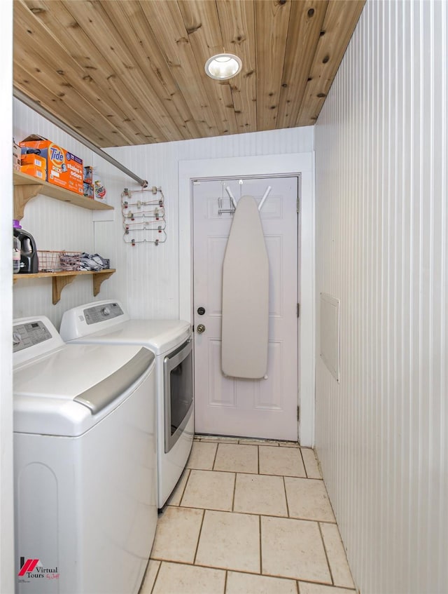 clothes washing area featuring wood walls, light tile patterned floors, washing machine and clothes dryer, and laundry area