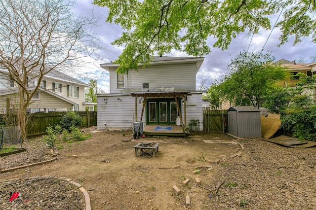 back of house with a deck, an outdoor fire pit, a fenced backyard, an outdoor structure, and a storage unit