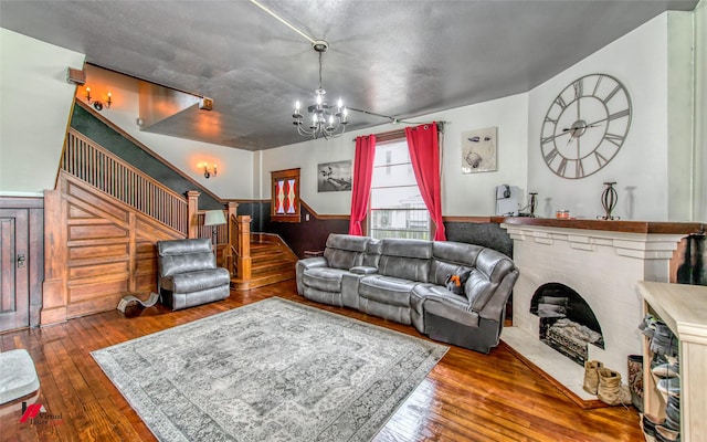living room featuring a wainscoted wall, a notable chandelier, wood-type flooring, and stairs
