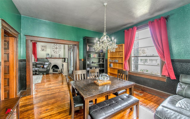 dining space with a fireplace with raised hearth, a notable chandelier, visible vents, a textured wall, and wood finished floors