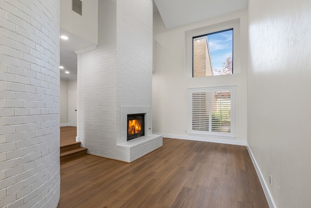 unfurnished living room featuring recessed lighting, a high ceiling, a brick fireplace, baseboards, and dark wood-style floors