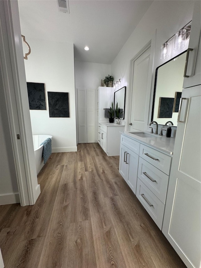 bathroom featuring visible vents, a sink, a soaking tub, wood finished floors, and two vanities