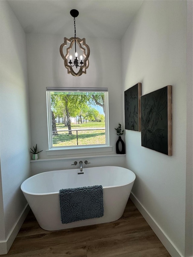 full bath with a chandelier, a freestanding bath, wood finished floors, and baseboards