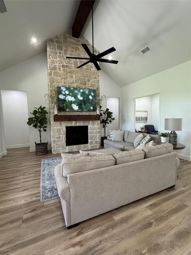 living room with visible vents, a stone fireplace, high vaulted ceiling, and baseboards