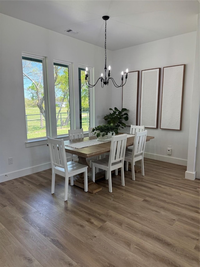 dining space featuring a chandelier, wood finished floors, baseboards, and visible vents