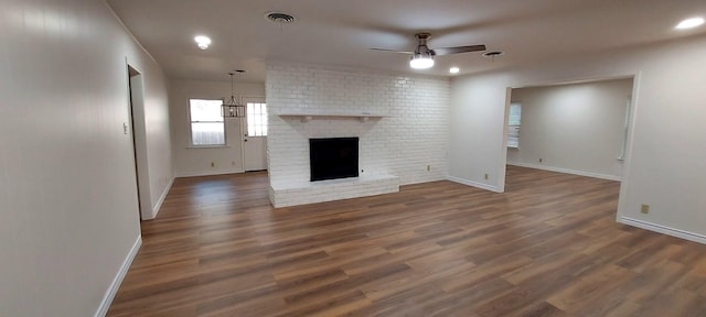 unfurnished living room with ceiling fan with notable chandelier, a fireplace, wood finished floors, and baseboards
