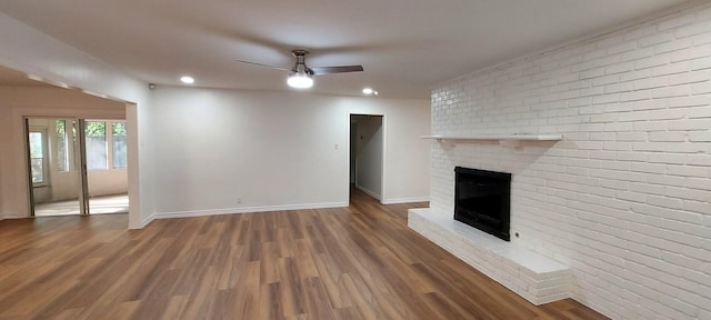 unfurnished living room with baseboards, a fireplace, wood finished floors, a ceiling fan, and brick wall