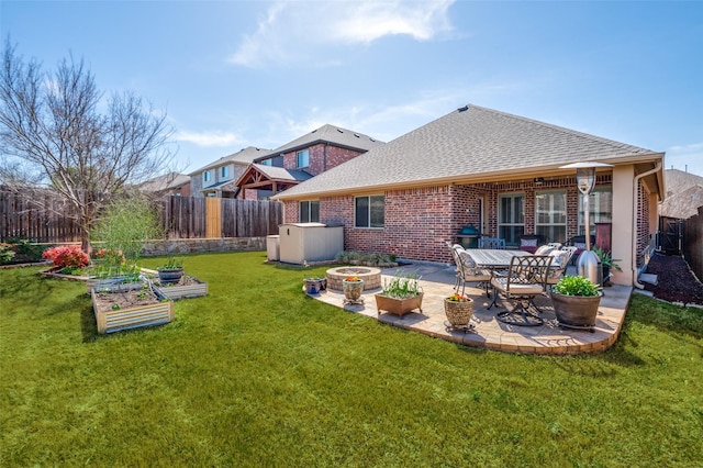 1001 Hodge St, Mckinney, TX 75071 - back of property featuring a garden, an outdoor fire pit, a patio area, a shingled roof, and brick siding