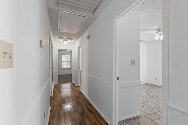 corridor featuring wood finished floors, a textured ceiling, attic access, and visible vents