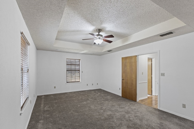 carpeted spare room featuring a textured ceiling, visible vents, baseboards, ceiling fan, and a raised ceiling
