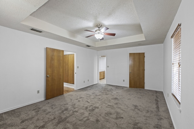 unfurnished bedroom featuring a tray ceiling, baseboards, visible vents, and carpet floors