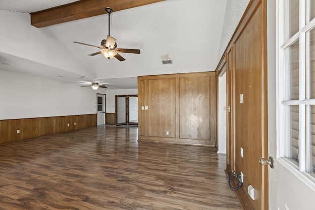 empty room with a wainscoted wall, visible vents, ceiling fan, dark wood-style floors, and vaulted ceiling with beams