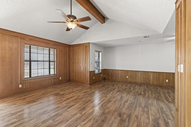 empty room with a ceiling fan, vaulted ceiling with beams, a textured ceiling, and wood finished floors