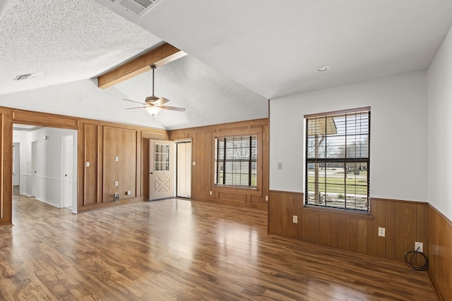 unfurnished living room featuring lofted ceiling with beams, a wainscoted wall, ceiling fan, visible vents, and wood finished floors