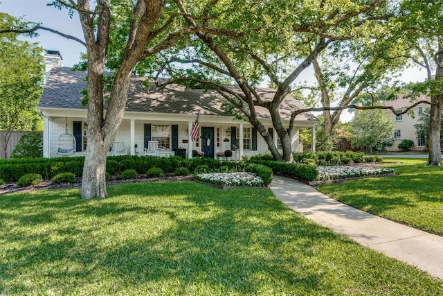 view of front of home with roof with shingles, a porch, a chimney, brick siding, and a front yard
