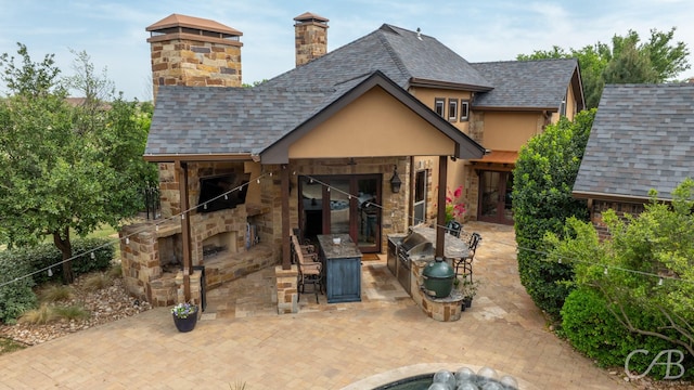rear view of property featuring a chimney, stone siding, french doors, an outdoor stone fireplace, and a patio