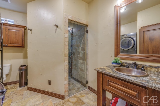 bathroom with a shower stall, toilet, vanity, baseboards, and washer / clothes dryer